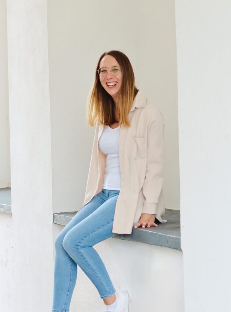 Sabrina sitzt auf einer Mauer und schaut lachend in die Kamera.